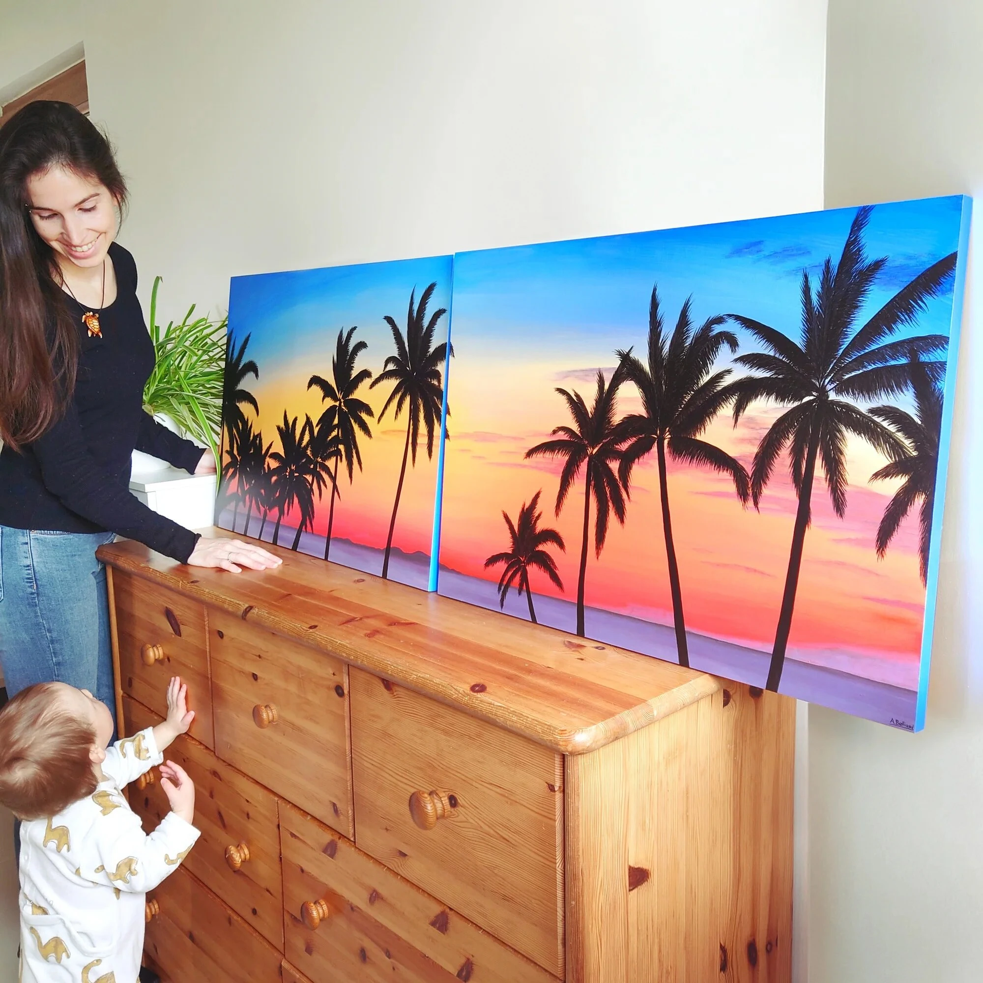 aline belliard, artiste peintre, et son grand tableau coucher de soleil avec des palmiers.