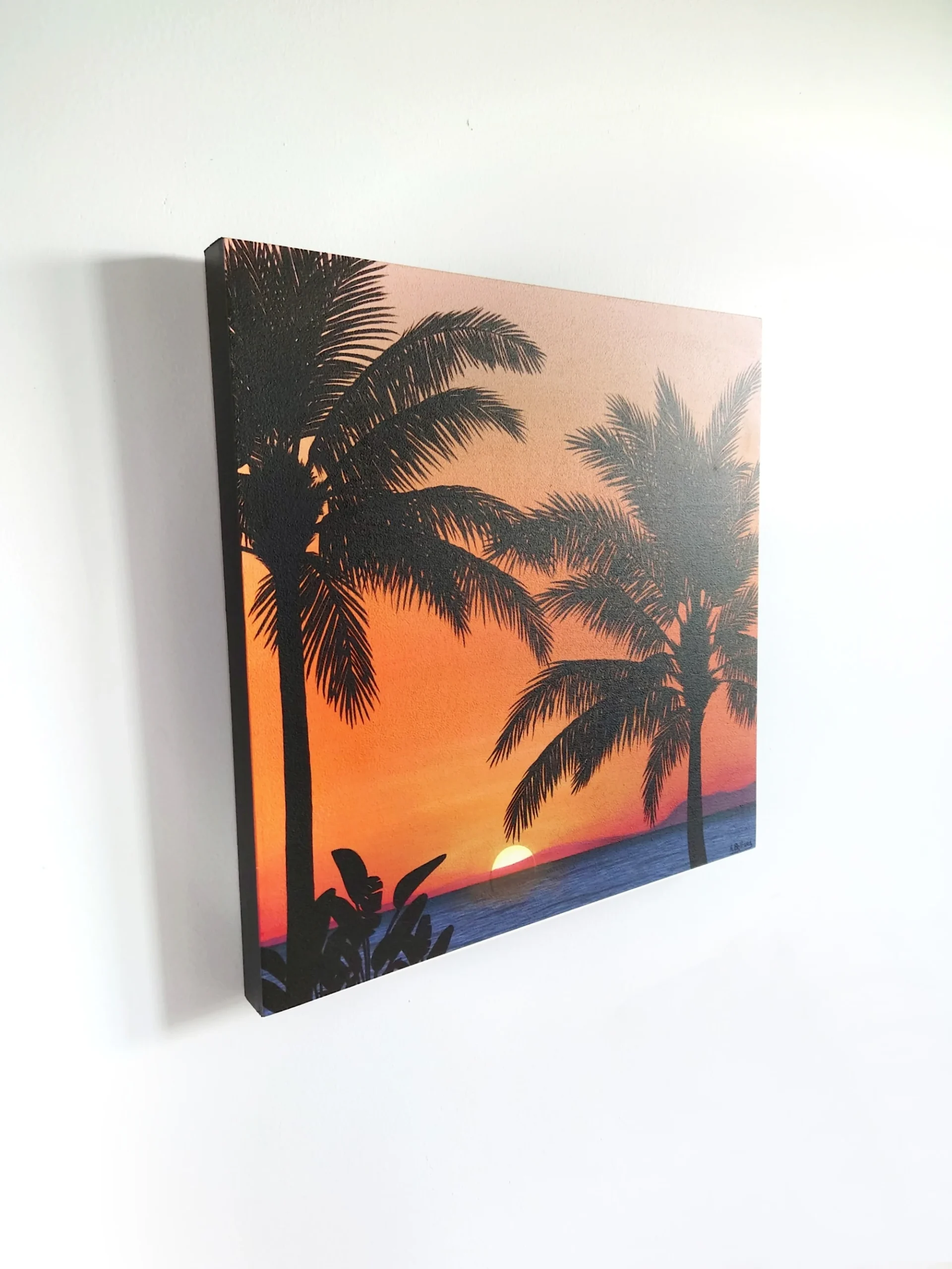 Petit tableau d'un coucher de soleil orange sur une plage de palmiers de taille 30x30 cm accroché sur un mur.