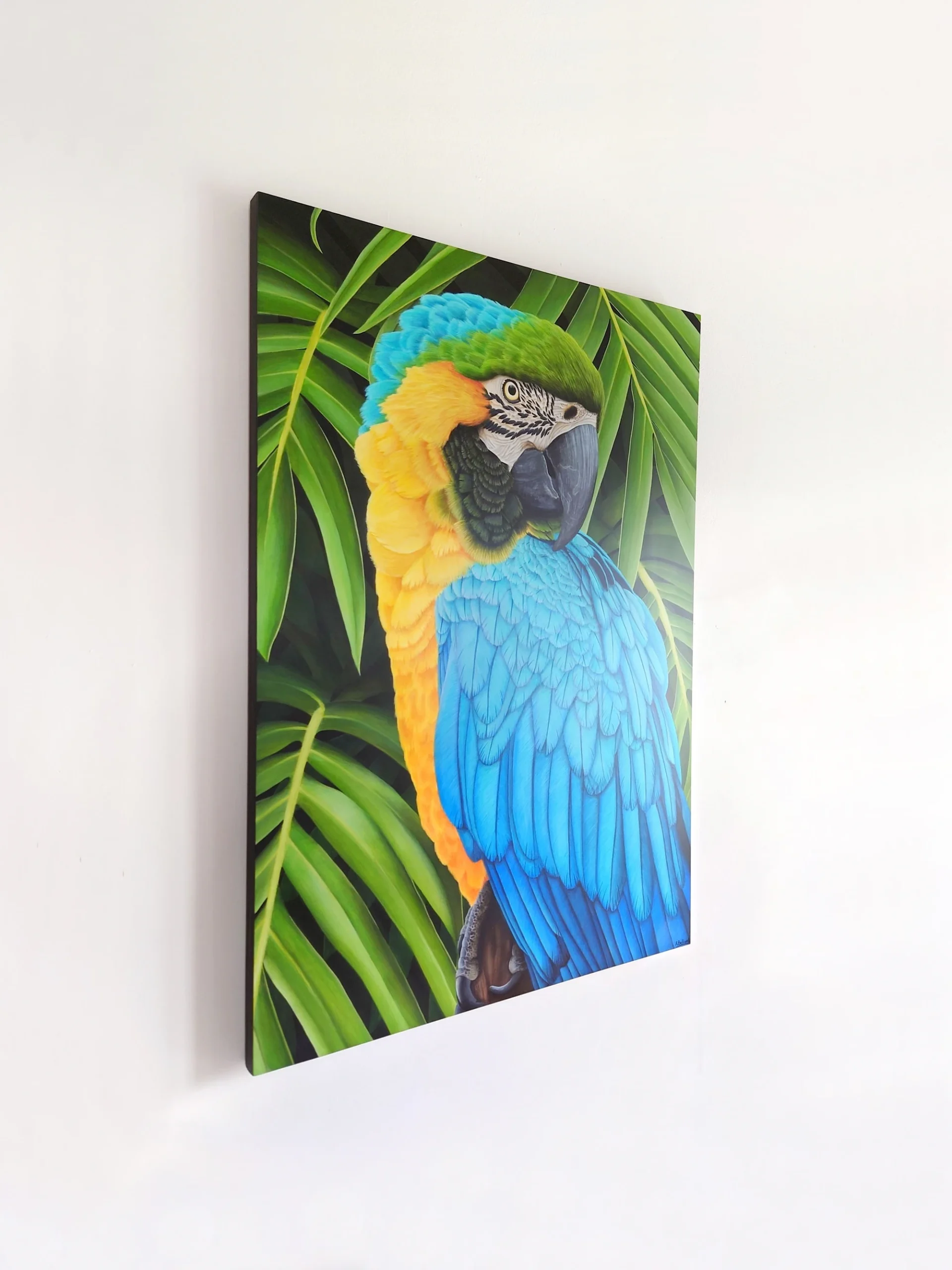 Grand tableau d'un oiseau tropical, perroquet ara ararauna, dans les feuillages de la forêt tropicale de taille 70x50 cm accroché sur un mur.