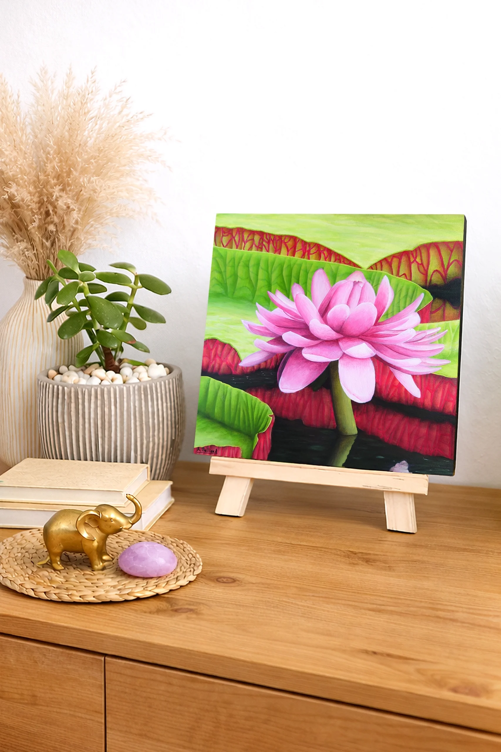 Peinture réaliste d’une fleur de nénuphar rose posée sur un petit chevalet dans une décoration naturelle et apaisante.