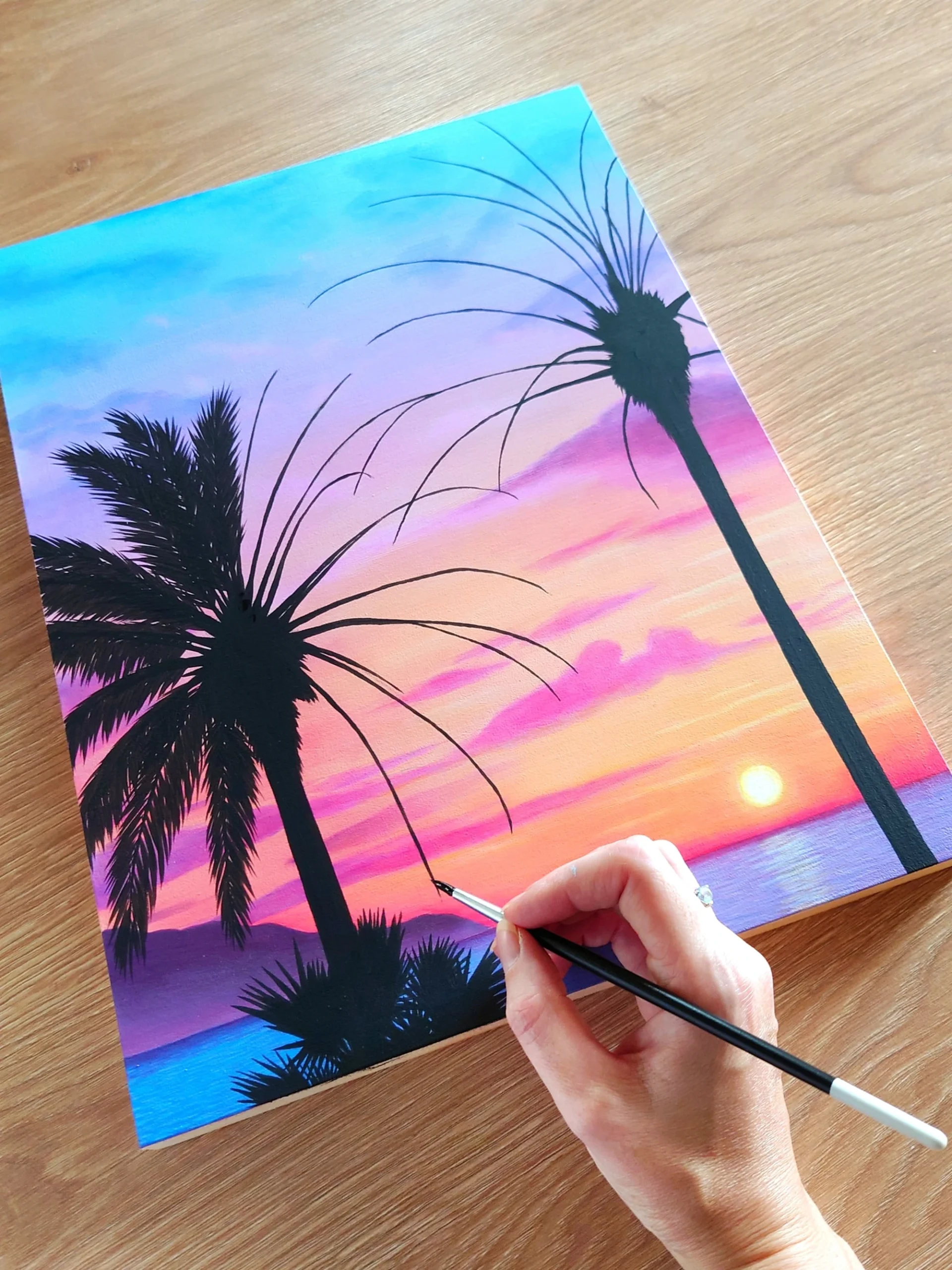 Peinture acrylique d'un coucher de soleil sur la mer, avec des palmiers devant sur bois naturel monté sur châssis par Aline Belliard