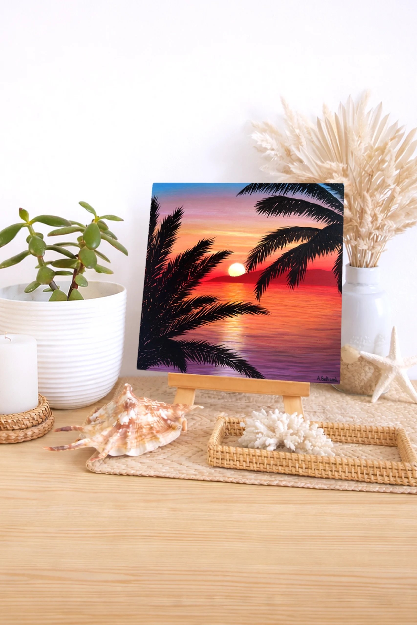 Peinture d’un coucher de soleil tropical sur l’océan avec palmiers en silhouette posée sur un meuble dans une décoration bord de mer.