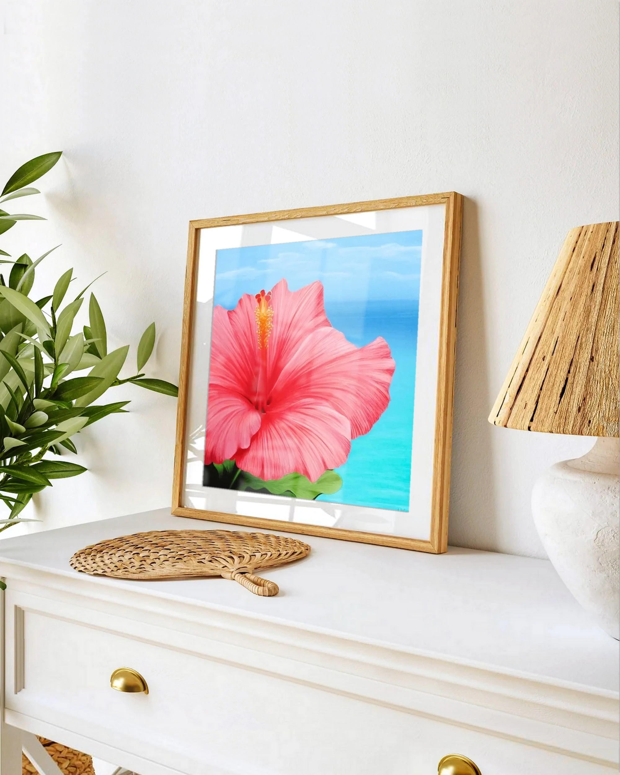 Affiche d'art d'une peinture de fleur d'hibiscus rose devant l'océan posée sur un meuble pour une décoration bord de mer exotique