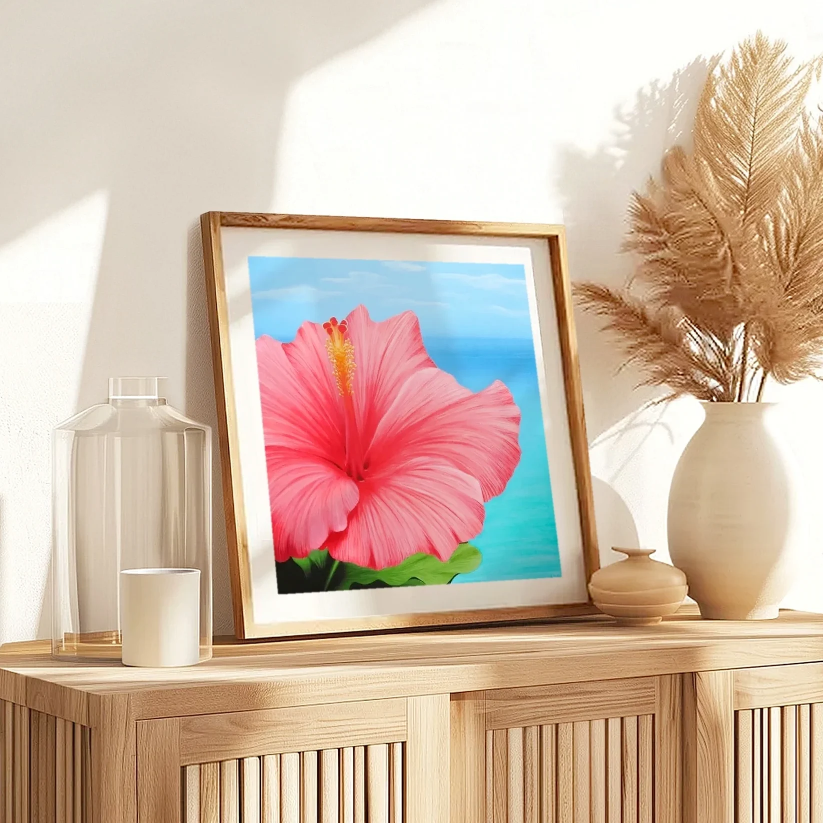 Impression d'art d'une peinture de fleur d'hibiscus rose devant l'océan posée sur un meuble pour une décoration bord de mer exotique